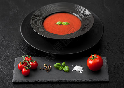 黑餐厅盘子背景的奶油番茄汤还有石板生番茄胡椒和盐图片