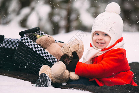 穿红色大衣的女孩在雪地里玩泰迪熊背景图片