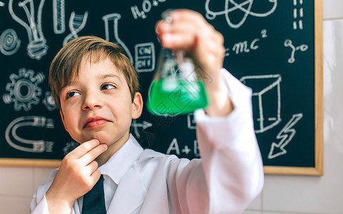 学习者深思熟虑的男孩打扮成化学家酒瓶在黑板前背景