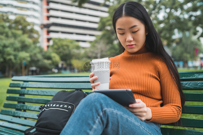 年轻女使用数码平板电脑在公园户外举杯咖啡图片