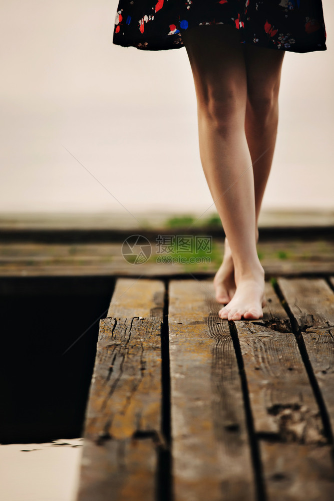 女孩赤脚走在通往湖边的木桥上图片