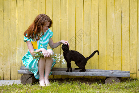 女孩和黑猫在靠着黄墙的凳子上图片