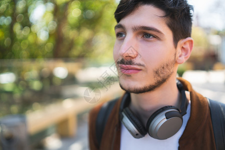 年轻拉丁男子在街上用耳机户外听音乐的肖像城市概念图片