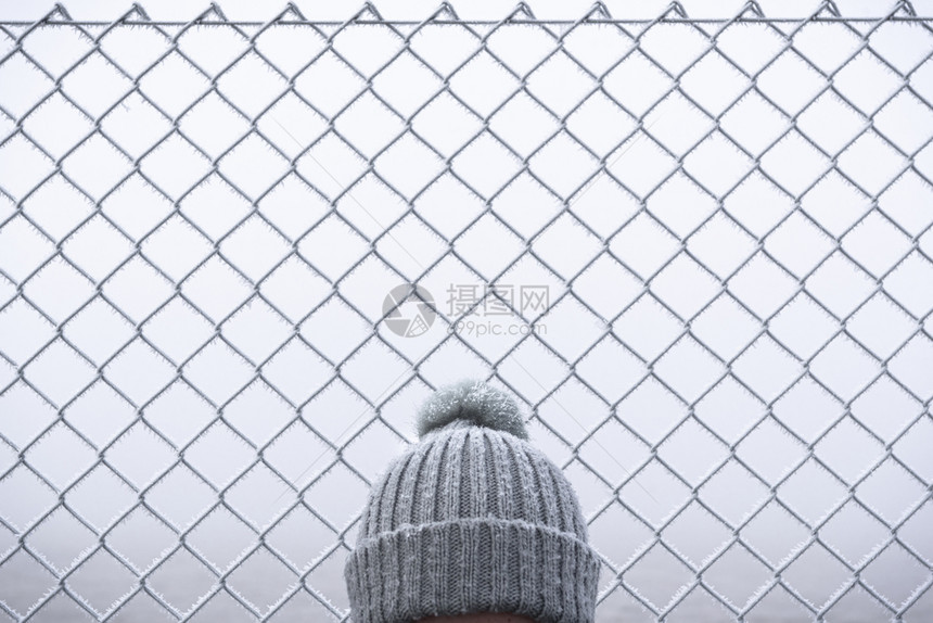 女人和头戴雪帽在寒冷的月桂日冬帽只贴近冷冻的铁丝网背景图片