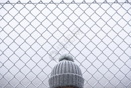 女人和头戴雪帽在寒冷的月桂日冬帽只贴近冷冻的铁丝网背景图片