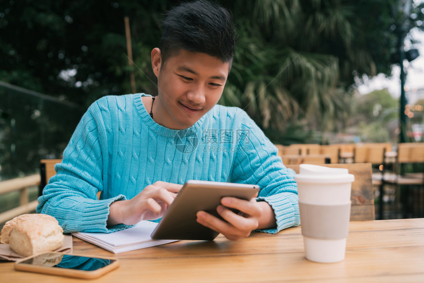 年轻亚洲人坐在咖啡店里时使用数码平板电脑学习的肖像技术概念图片