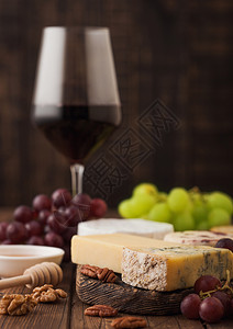 玻璃红葡萄酒在板上挑选各种奶酪和木制桌底的葡萄图片