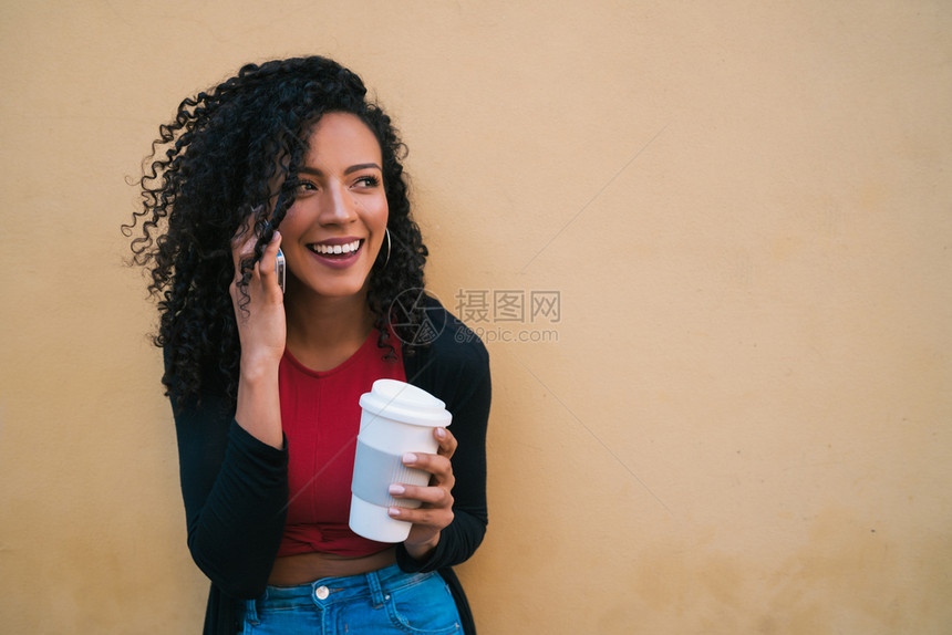 afro年轻女在黄色背景下举杯咖啡时在电话上聊天的肖像图片