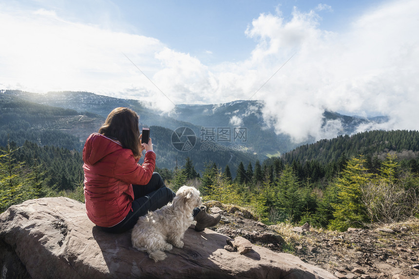 年轻女子与她的狗喜欢黑森林山在一个阳光明媚的春天在德国女孩用手机拍照假期概念图片