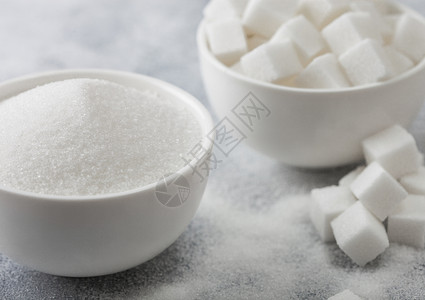 天然白糖立方体和浅底精制糖的白色碗盘背景图片