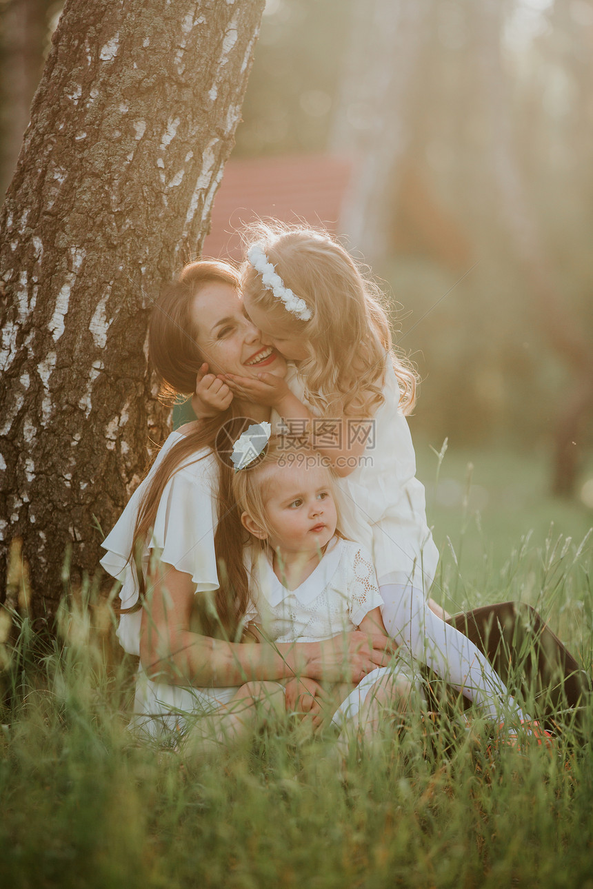 快乐的家庭妈和两个可爱的女儿坐在草地上图片