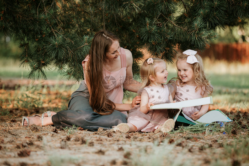 两名小女孩的户外肖像正在和母亲一起阅读本关于草地的书图片