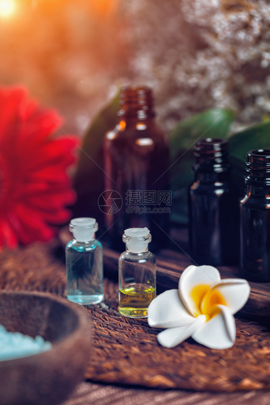 含蓝色和绿基本油的透明芳香药瓶垂直疗法构成白花和红装饰木碗中的蓝海盐芳香疗法的放松概念图片