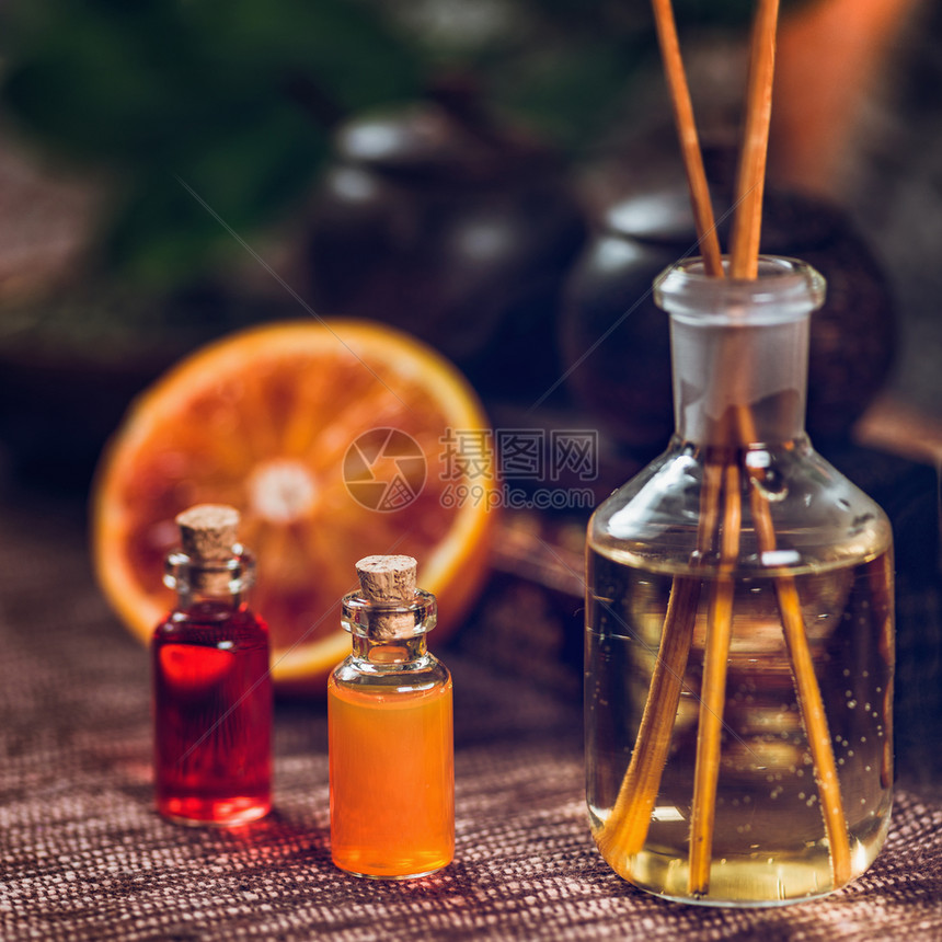 装满红色和橙基本油芳香药瓶的子里面有木棍新鲜柑橘水果被切成两半图片
