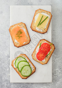 各种健康的饼干有鲑鱼和奶酪西红柿黄瓜大理石板上有背景为浅色桌图片