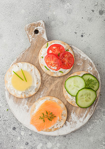 各种圆形健康饼干配有鲑鱼和奶酪番茄黄瓜放在浅色桌底的木切面板上图片