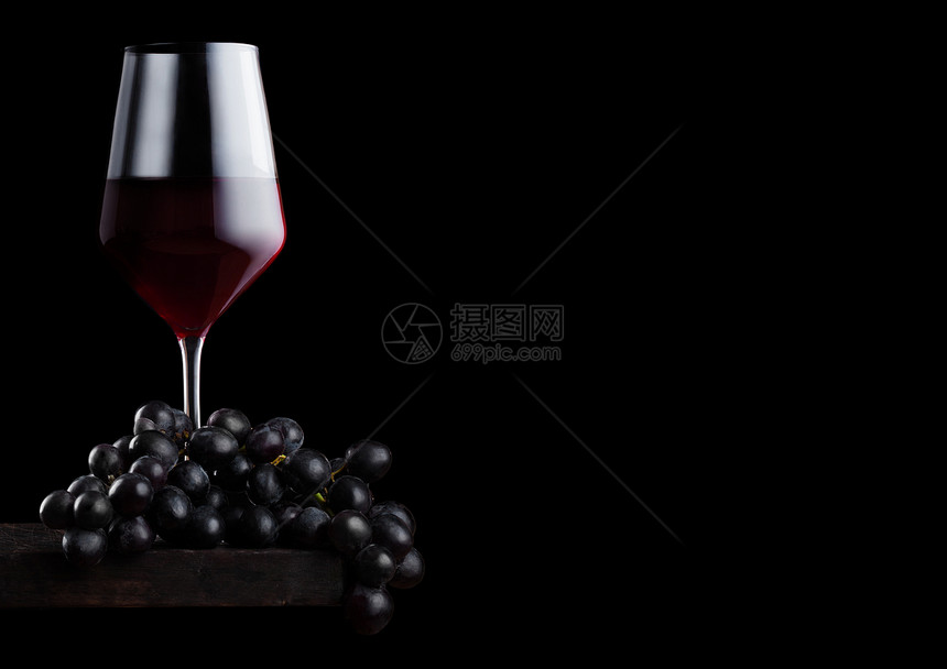 黑色背景的木板上装着深葡萄的优雅红酒杯图片