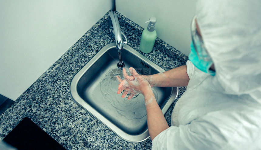 无法辨认身着细菌保护西装的妇女双手用肥皂洗图片