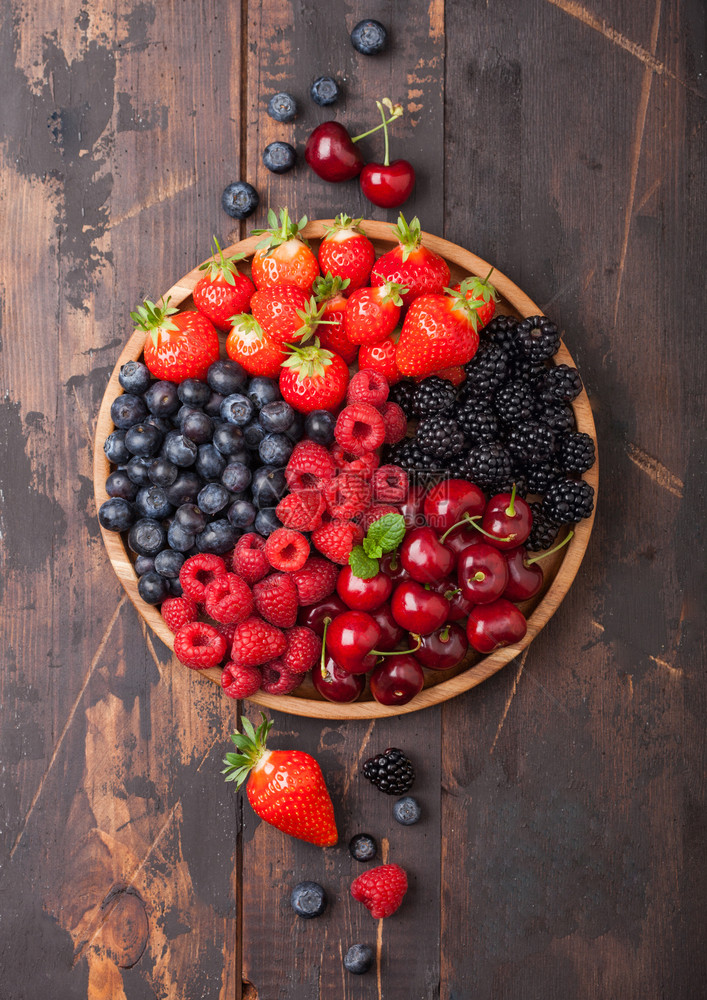 黑木桌底的圆盘中新鲜有机夏季果子混合物草莓蓝黑和樱桃图片