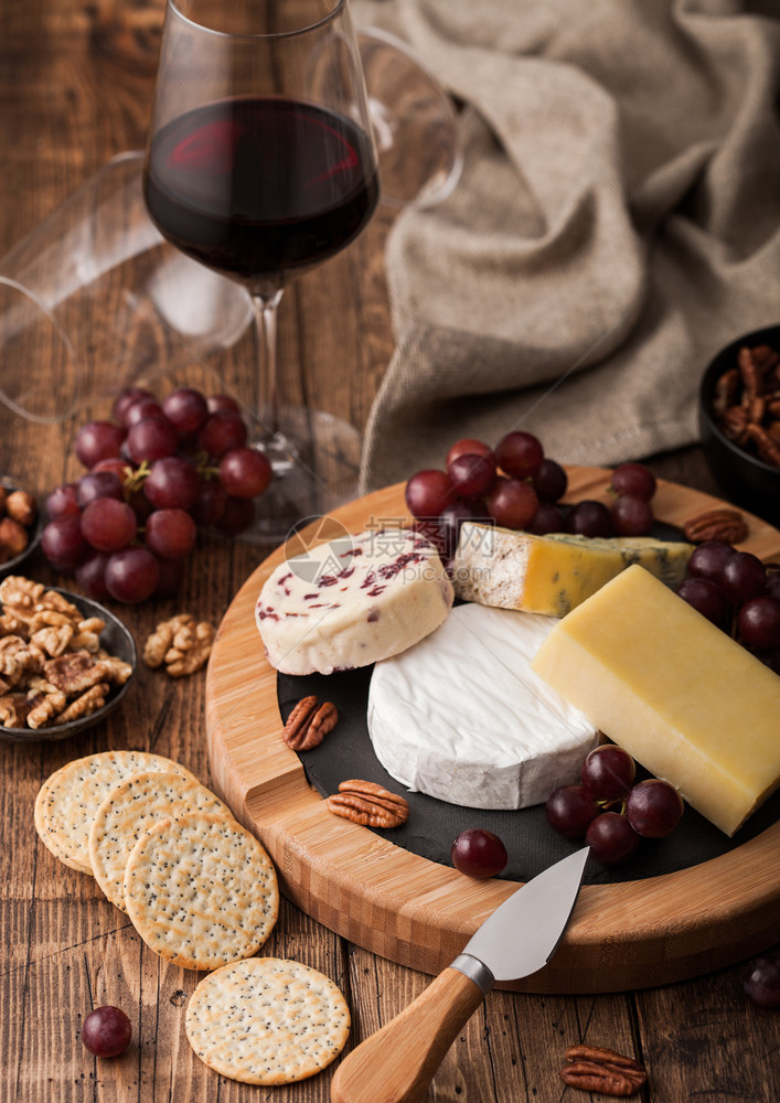玻璃红葡萄酒在板上挑选各种奶酪和木制桌底的葡萄图片