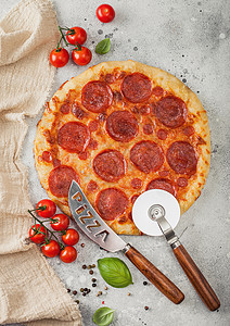 奶酪轮新鲜的圆烤意大利披萨配有切轮刀和子配有西红柿和在轻便厨房餐桌背景上的烤肉背景