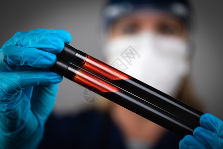 身戴医疗面罩的女实验室工人在黑暗背景下持有血液测试管图片