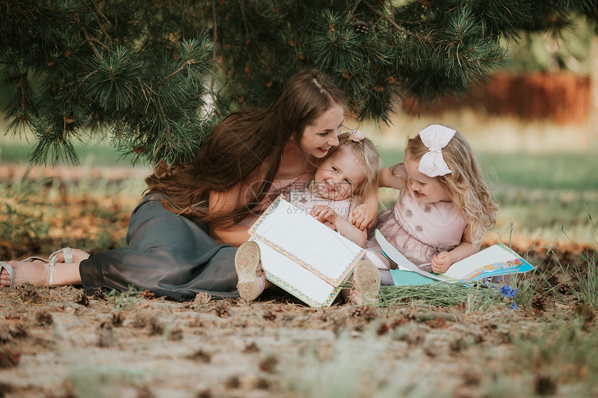 幸福的家庭母亲和两个女儿母亲和两个女儿坐在草地上看一本书母亲和两个女儿在白天的概念图片