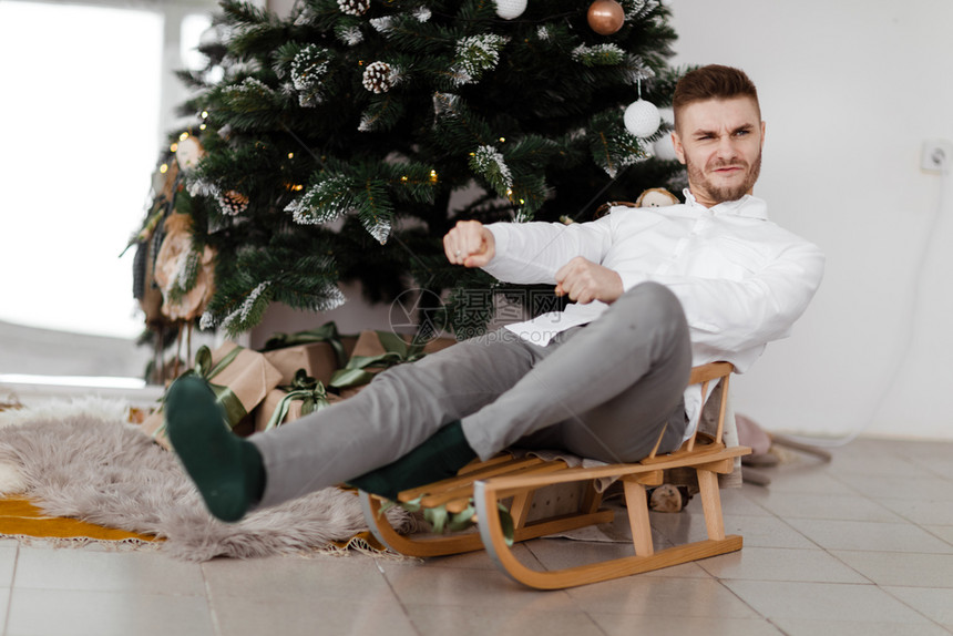男子坐在家中圣诞树旁的雪橇上图片