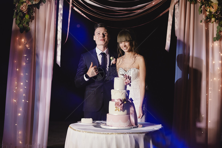 新娘和新郎站在婚礼蛋糕旁图片