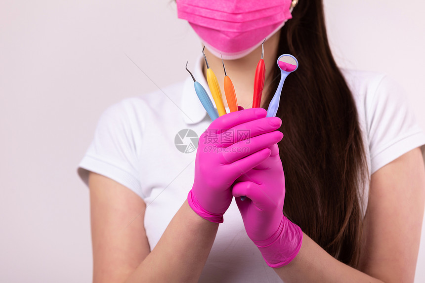 人医药牙科和保健概念穿粉红色面罩的牙医妇女白底带彩色工具的医疗手套图片