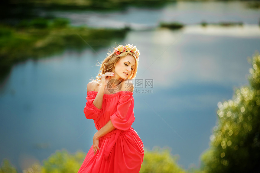 美丽的年轻金发女郎头戴花圈美丽的女孩头戴花圈漂亮的女孩头戴花圈漂亮的环美丽女孩面戴红色花圈湖附近的红长裙时装照片空间美丽的女孩面图片