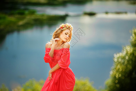 美丽的年轻金发女郎头戴花圈美丽的女孩头戴花圈漂亮的女孩头戴花圈漂亮的环美丽女孩面戴红色花圈湖附近的红长裙时装照片空间美丽的女孩面背景图片