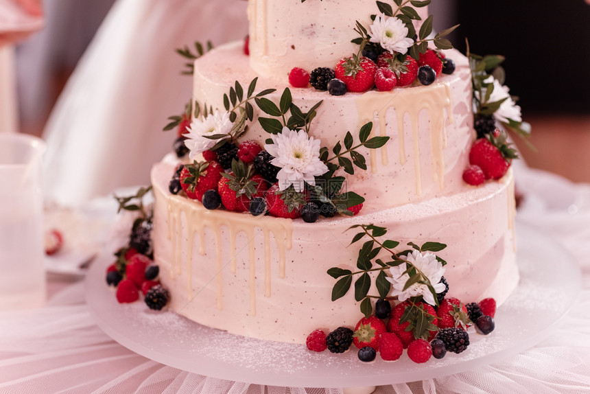 白蛋糕上装饰着浆果和白花在婚礼派对的桌子上结婚日图片