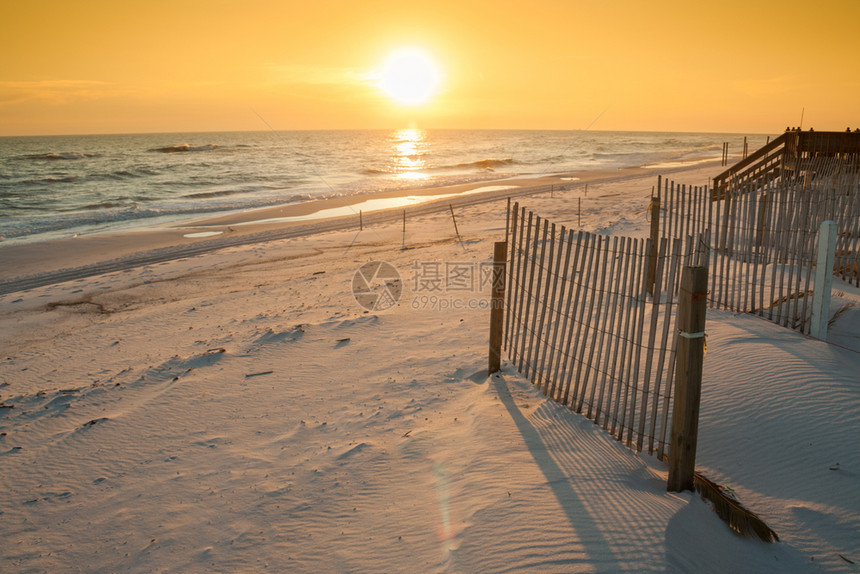 美丽的日落在海面上加沙子的栅栏图片