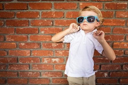 可爱的男孩戴着墨镜站在砖墙上图片