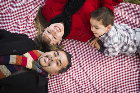 身着冬衣的青年混合种族家庭背靠在公园野餐毯上躺在公园里图片