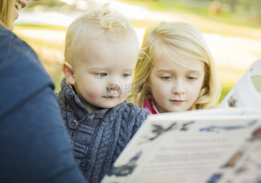 母亲在户外读了一本书给两个可爱的金发孩子图片