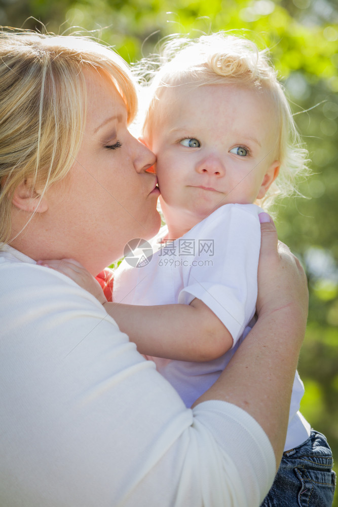 年轻妈亲吻把她可爱的男孩抱在公园里图片