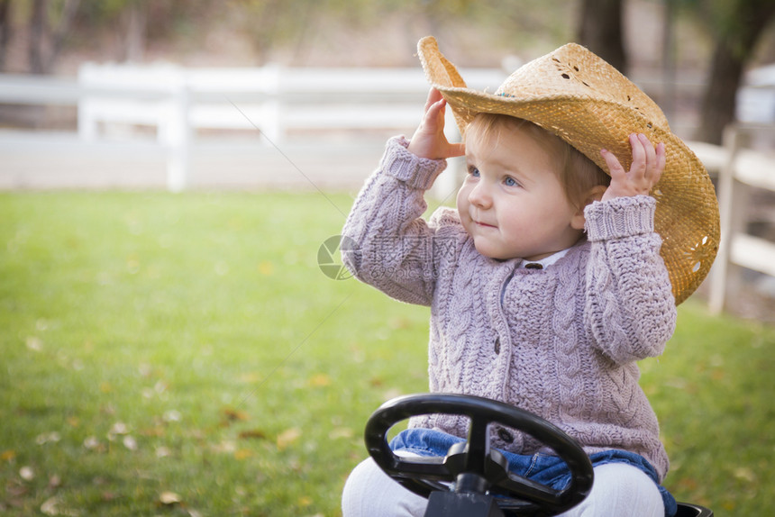 戴着牛仔帽的女孩开心的坐在玩具拖拉机上图片
