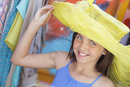 漂亮的年轻女孩在市场试戴黄帽子图片