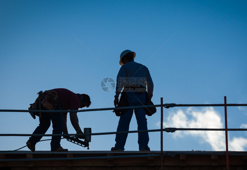 夕阳下建筑工人在屋顶上的背景图片