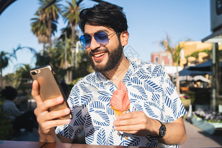年轻人在吃冰淇淋和户外使用手机时享受阳光灿烂的天气图片