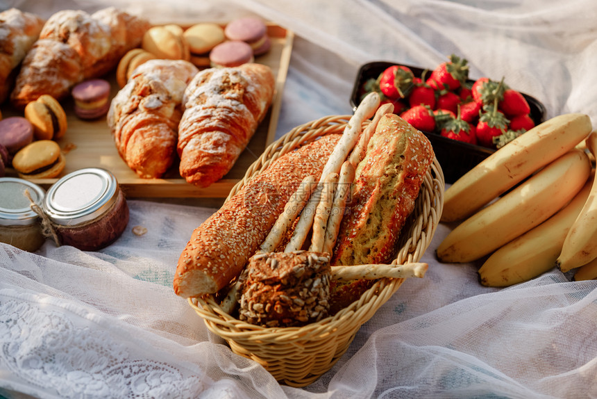 法国羊角面包和新鲜果子在草地上供养两个人面有粉红色的花瓣有选择焦点野餐在大自然新鲜的糕点羊角面包新鲜的果子法国羊角面包和新鲜果子图片