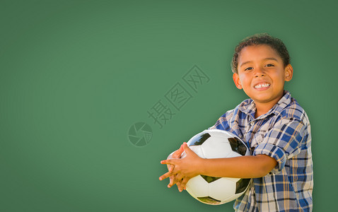 可爱笑的年轻混血男孩在白粉板前拿着足球图片