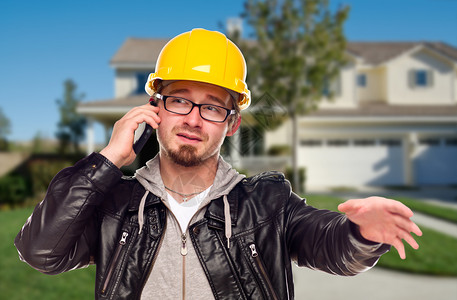 年轻承包商在家门口用手机戴硬帽背景图片