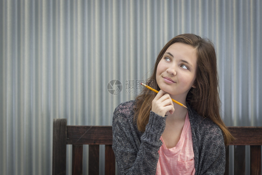 年轻漂亮的白日梦女学生用铅笔坐在长椅上看着一边图片