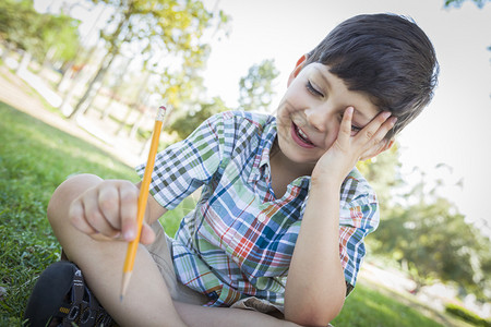 沮丧的可爱男孩拿着铅笔坐在草地的户外图片