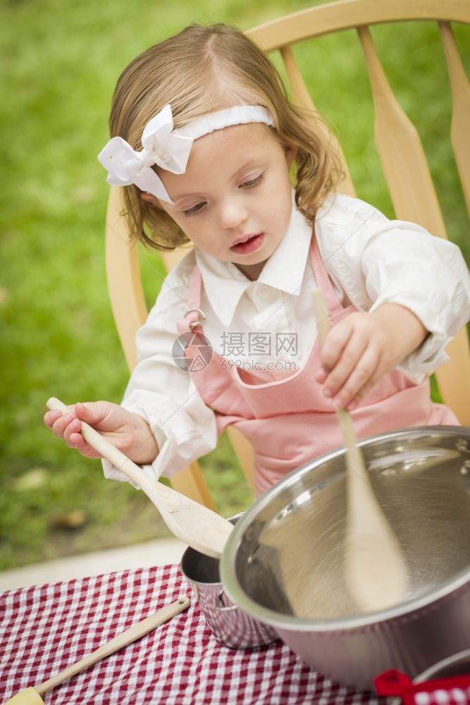 快乐可爱的小女孩玩厨师烹饪在她的粉红色服装图片