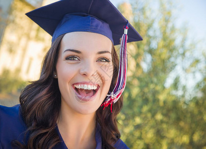 快乐毕业的混血女子穿着帽和礼服在校园庆祝图片
