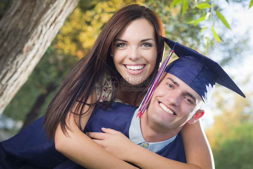 穿着帽子和礼服的快乐男毕业生和漂亮的女孩在外面庆祝图片